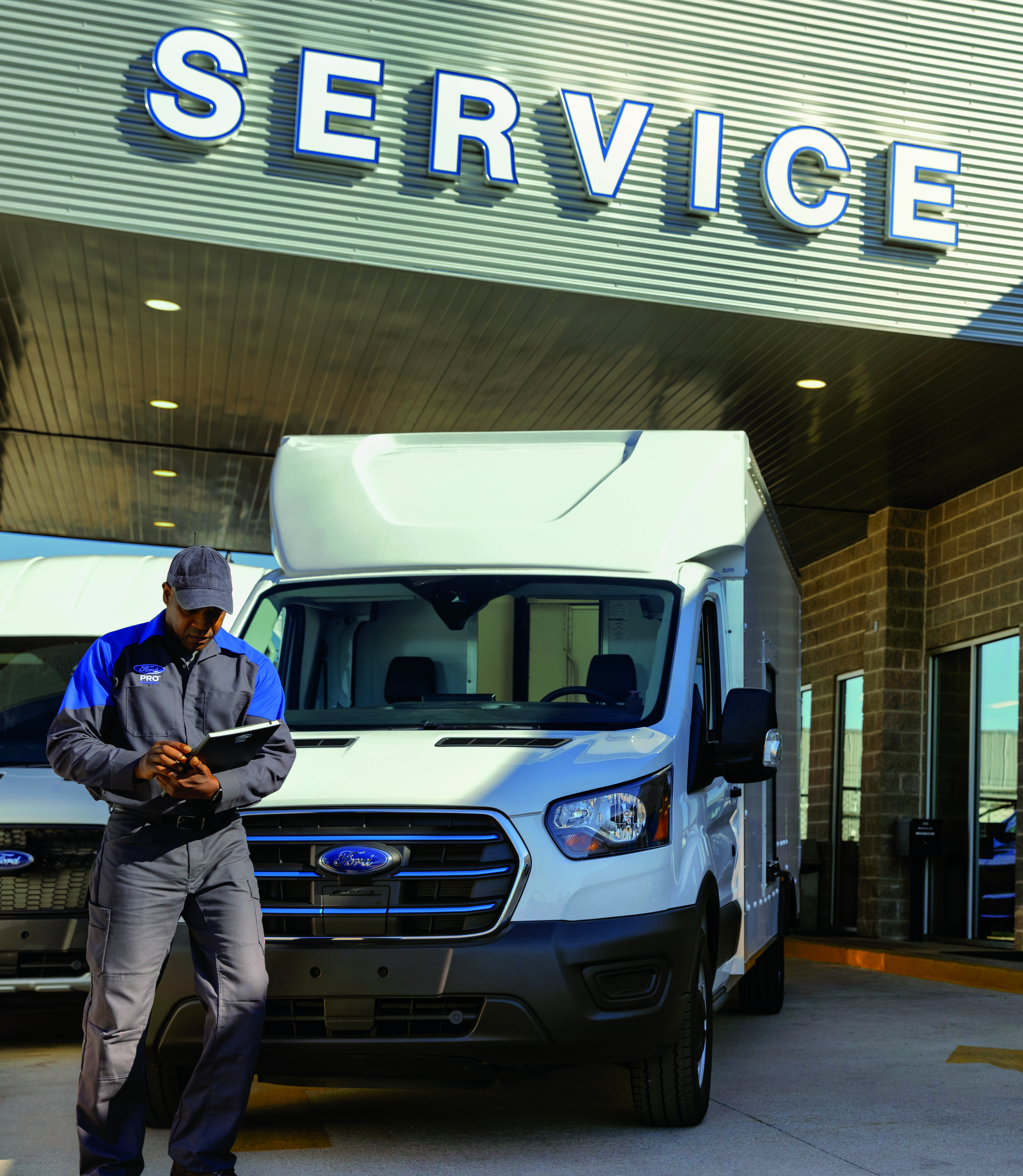 A man looks at a tablet in front of a work truck parked under an awning that says "service"